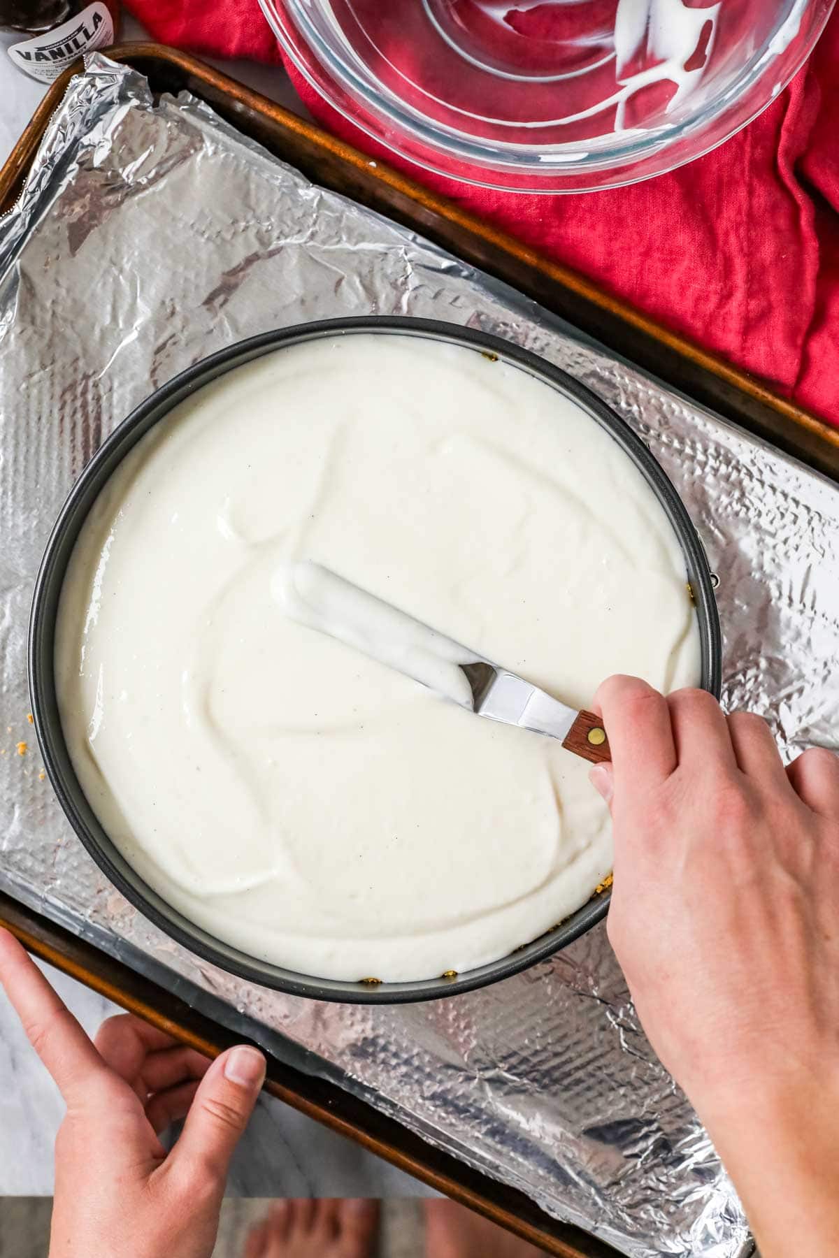 Overhead view of a sour cream topping being spread over a cheesecake.