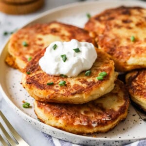 Plate of mashed potato pancakes made with leftover mashed potatoes topped with sour cream and chives.