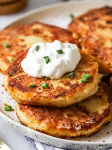 Plate of mashed potato pancakes made with leftover mashed potatoes topped with sour cream and chives.