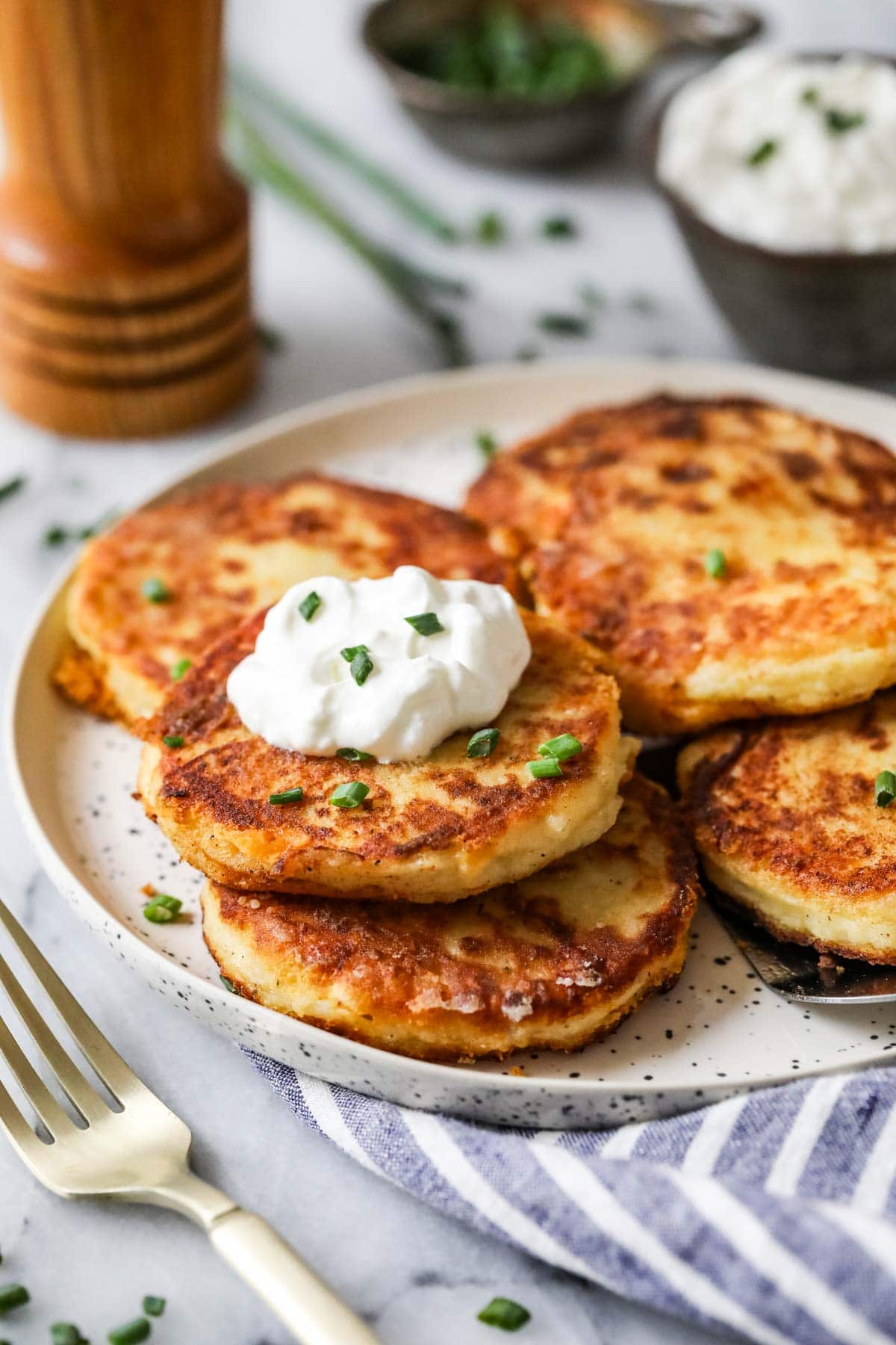 Plate of mashed potato pancakes made with leftover mashed potatoes topped with sour cream and chives.