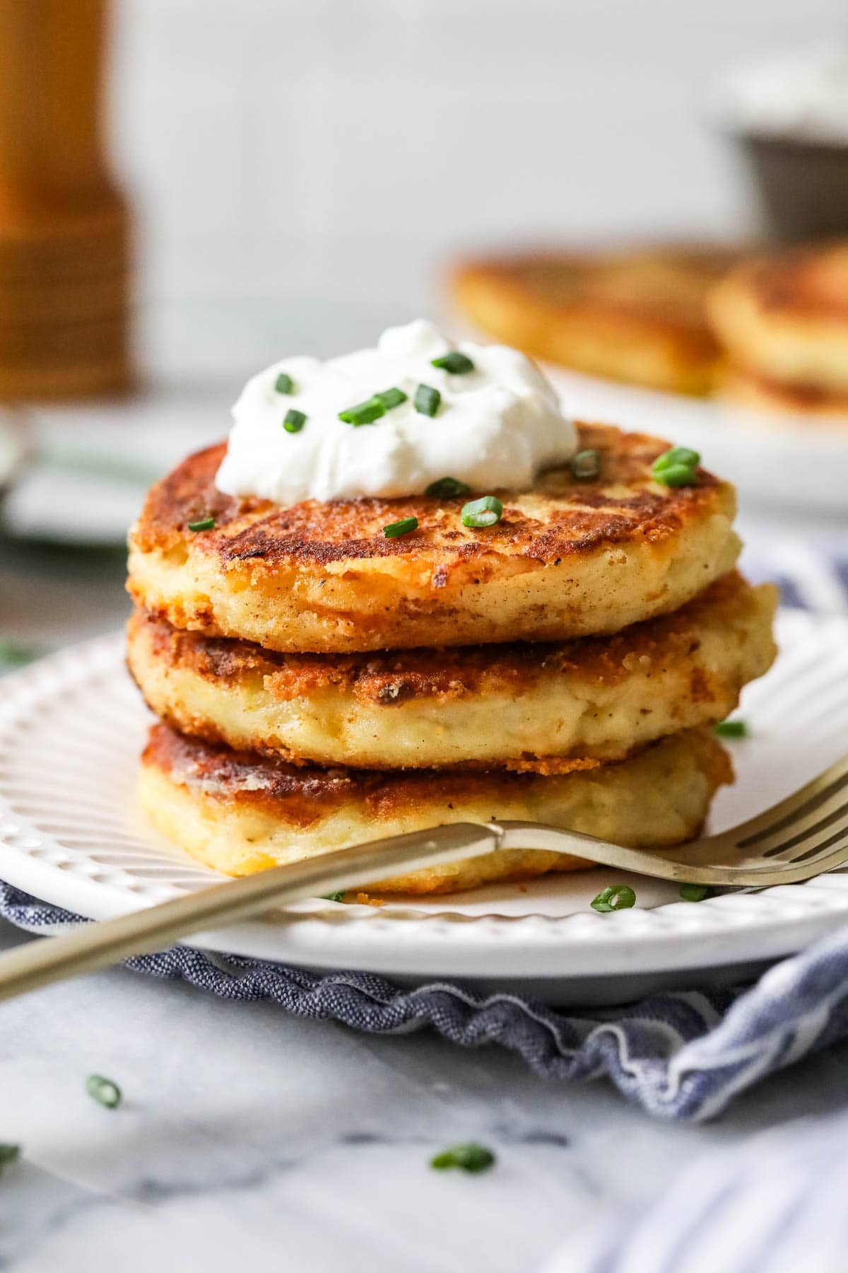 Stack of three mashed potato pancakes topped with sour cream and chives.