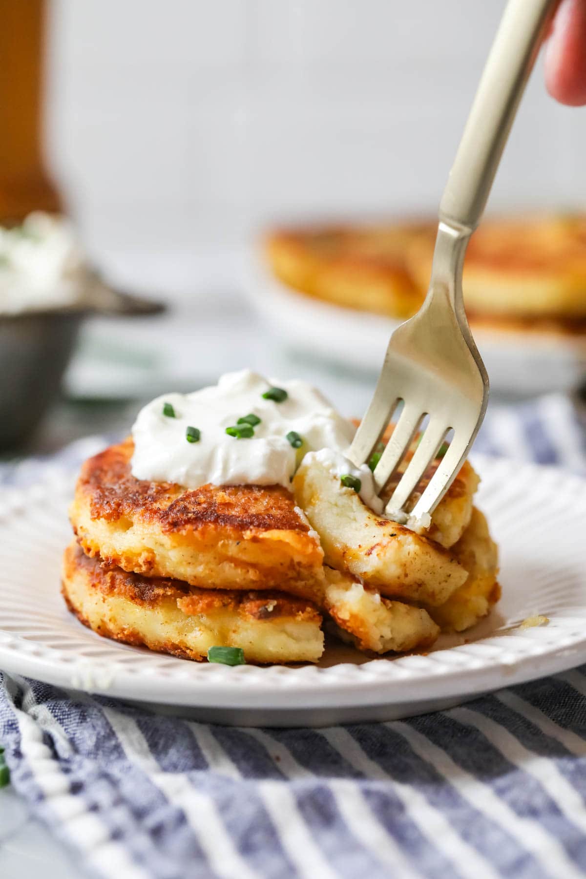 Fork taking a bite from a stack of potato pancakes topped with sour cream.