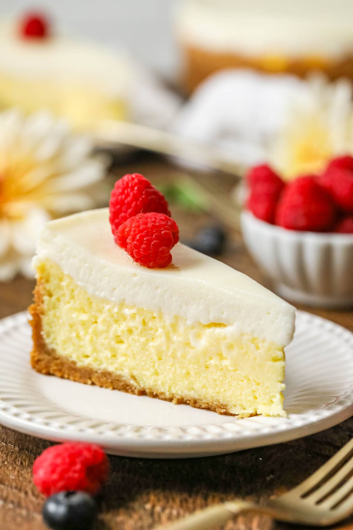 Slice of cheesecake made with a sour cream topping garnished with raspberries.