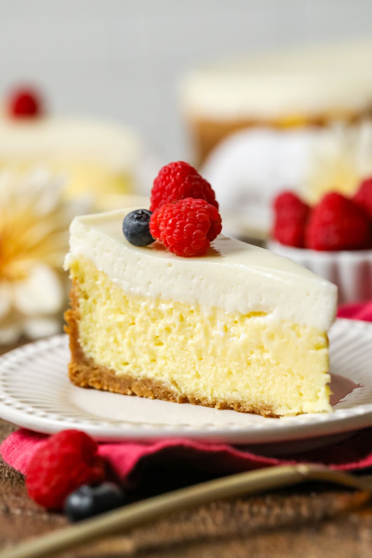 Slice of New York cheesecake with raspberries and a blueberry on top.