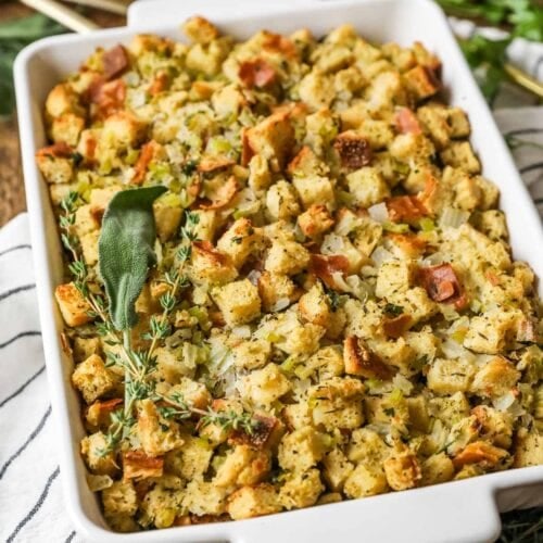 Overhead view of a casserole dish of stuffing topped with a bundle of fresh herbs.