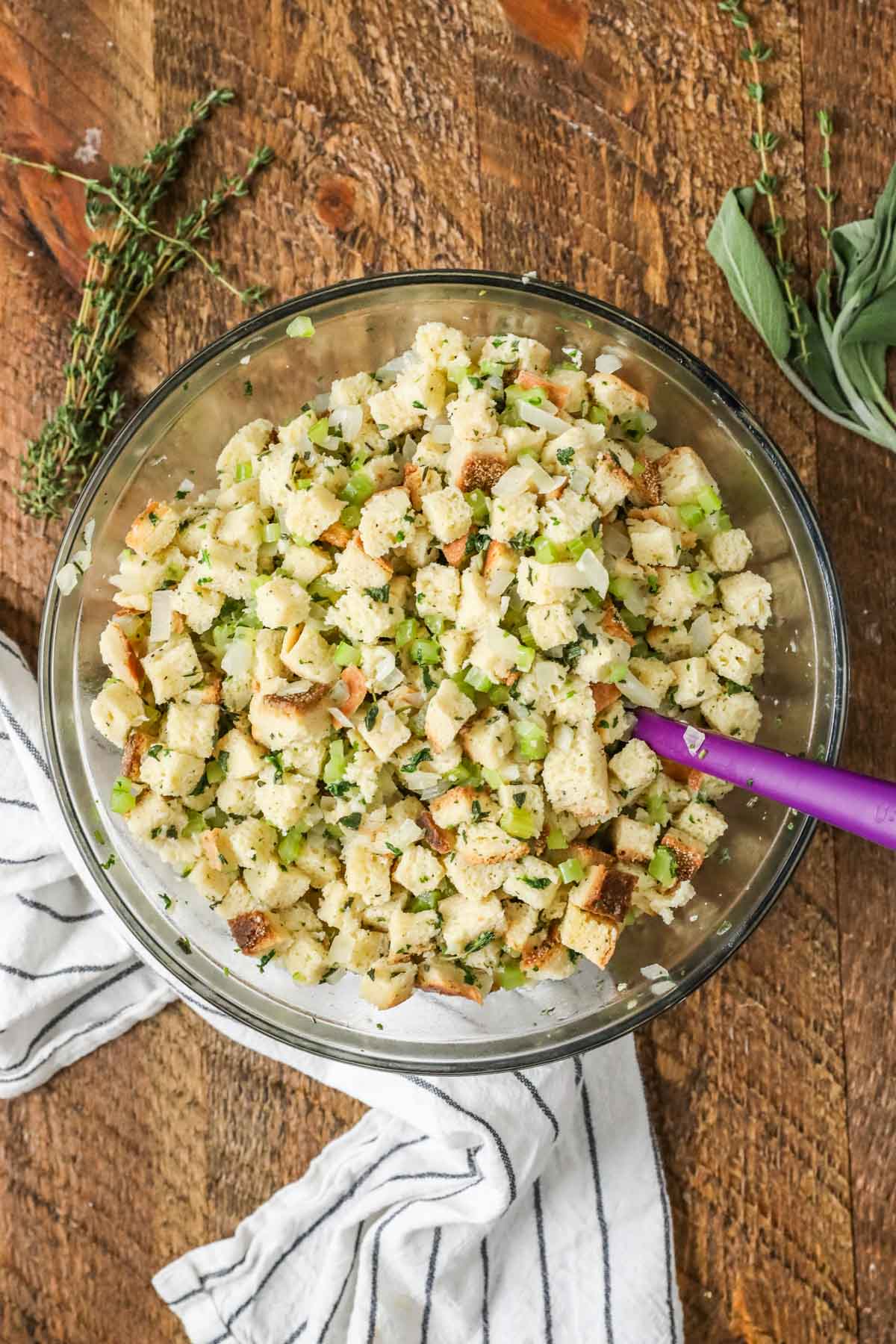 Overhead view of a bowl of bread cubes stirred together with herbs and veggies.