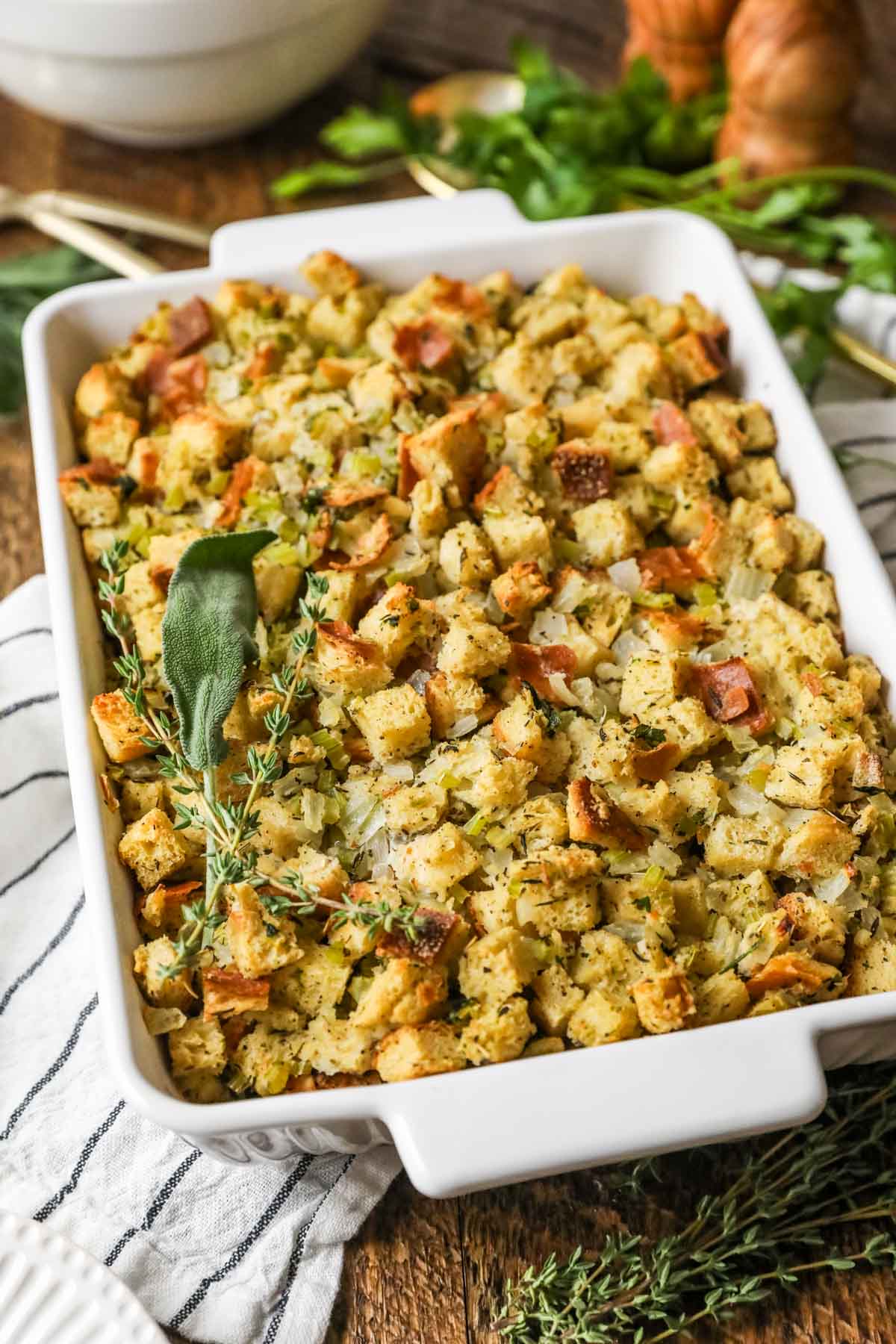 Overhead view of a casserole dish of stuffing topped with a bundle of fresh herbs.