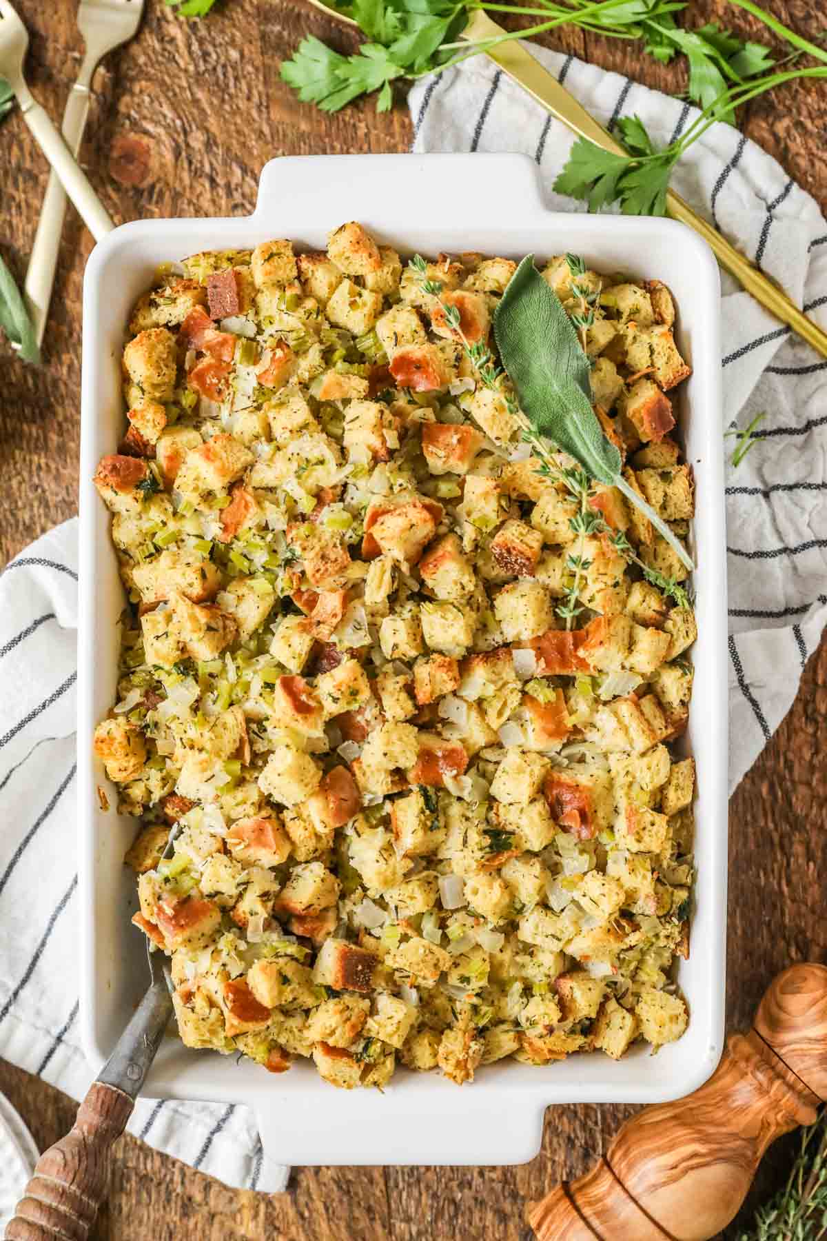 Overhead view of a casserole dish of stuffing topped with a bundle of fresh herbs.