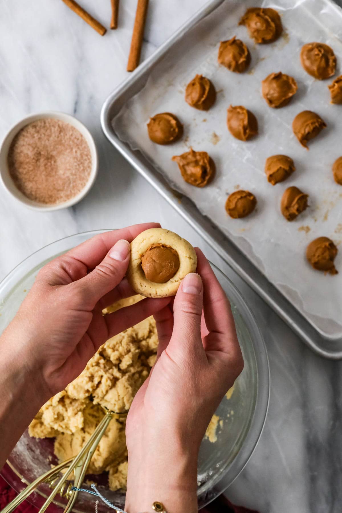 Hands forming cookie dough around a frozen cookie butter ball.