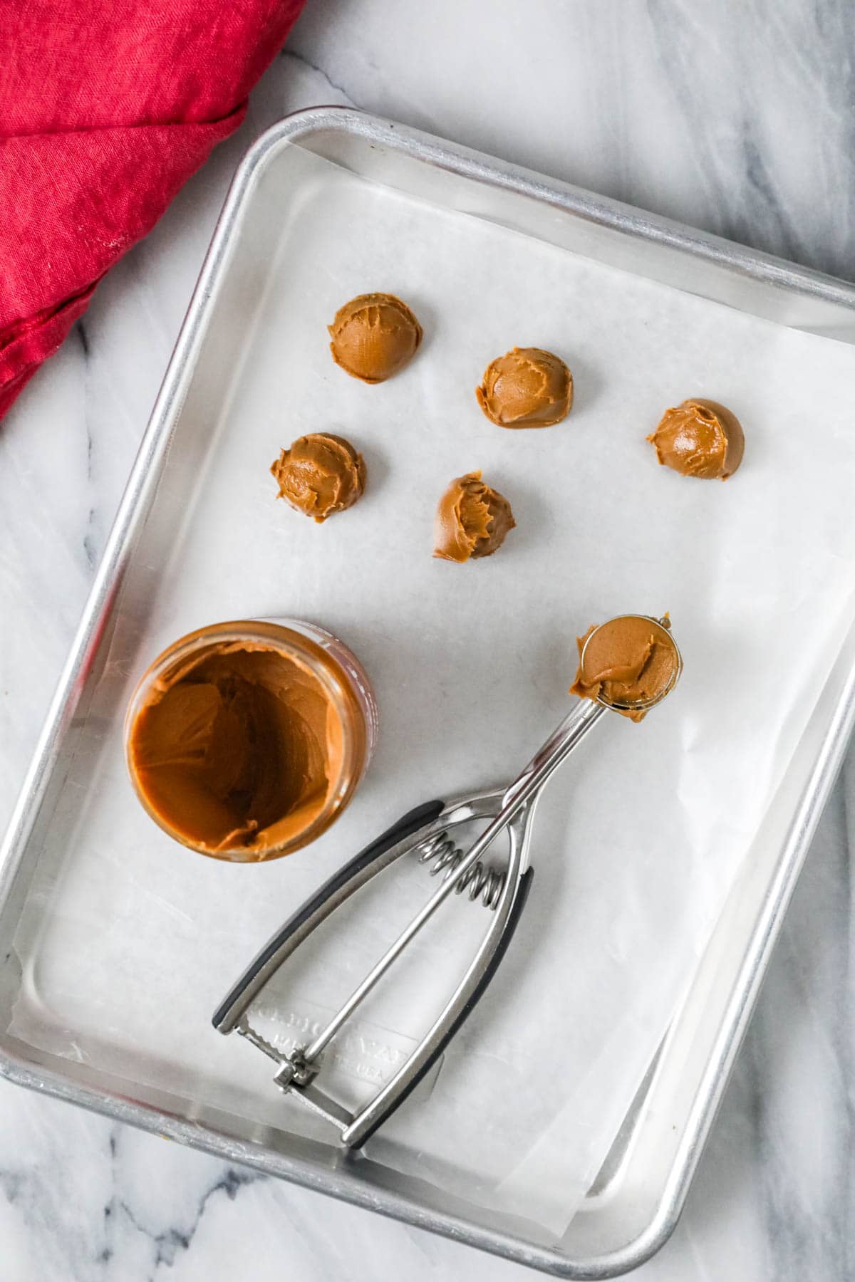 Overhead view of cookie butter scoops being dropped on a parchment lined baking sheet.