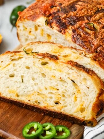 Slices of sourdough cheddar jalapeno bread resting beside the loaf on a cutting board.