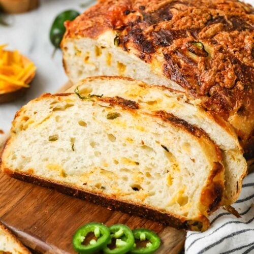 Slices of sourdough cheddar jalapeno bread resting beside the loaf on a cutting board.