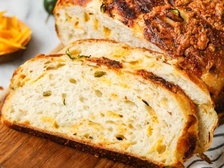 Slices of sourdough cheddar jalapeno bread resting beside the loaf on a cutting board.