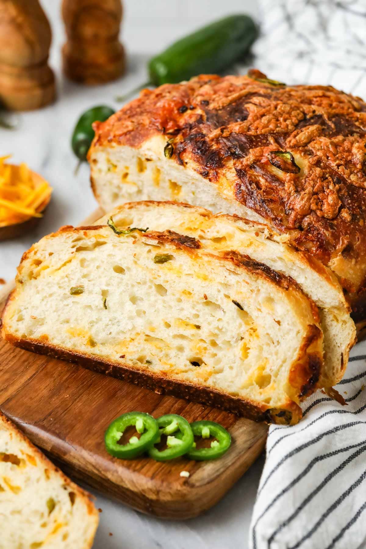 Slices of sourdough cheddar jalapeno bread resting beside the loaf on a cutting board.