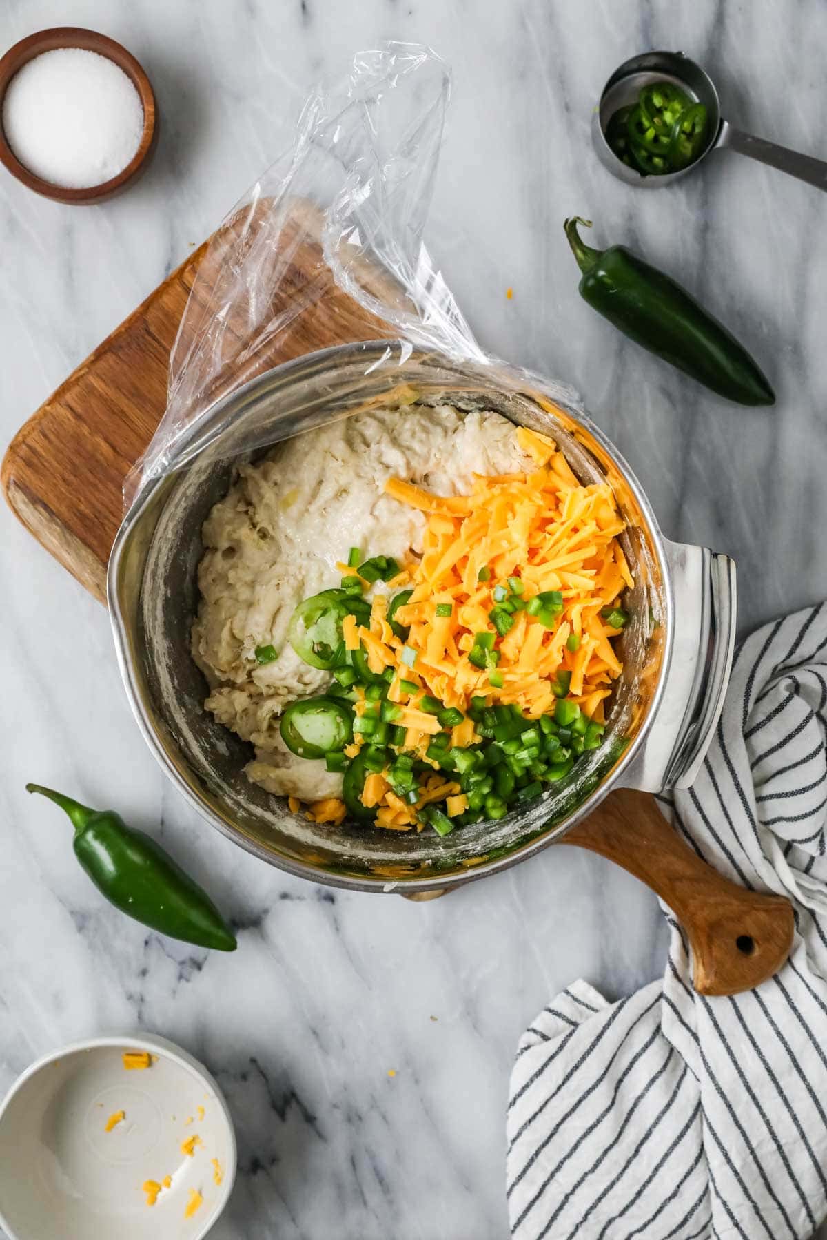 Overhead view of a mixing bowl with sourdough bread dough topped with shredded cheese and jalapenos.