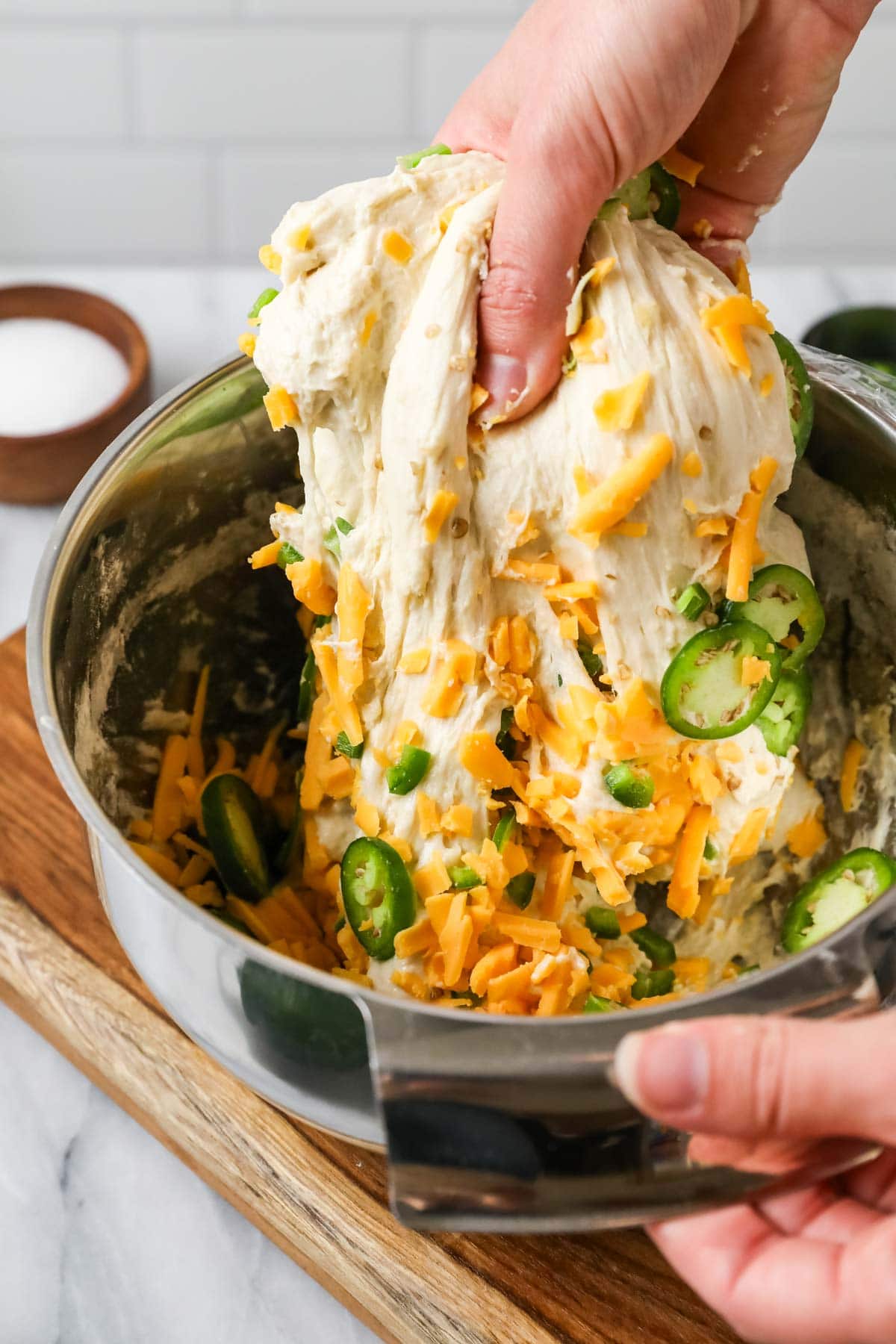 Hands stretching a cheddar jalapeno dough in a bowl.