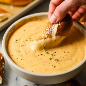 Pretzel being dipped into a bowl of beer cheese dip.