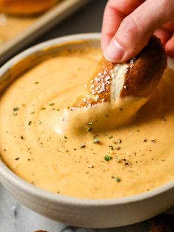 Pretzel being dipped into a bowl of beer cheese dip.