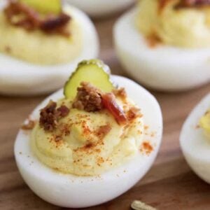 Deviled egg topped with bacon, paprika, and a pickle slice.