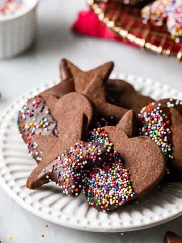 Plate of chocolate shortbread cookies that have been half dipped in chocolate and nonpareil sprinkles.