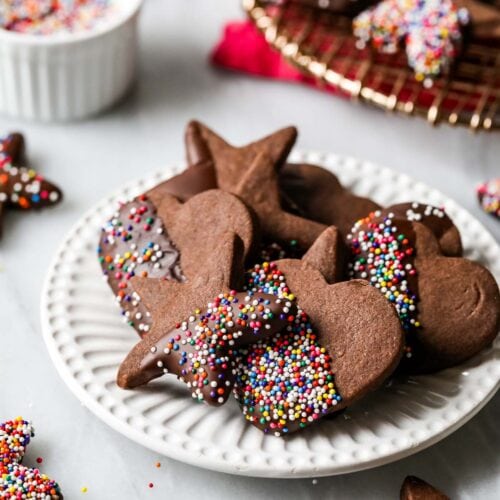 Plate of chocolate shortbread cookies that have been half dipped in chocolate and nonpareil sprinkles.