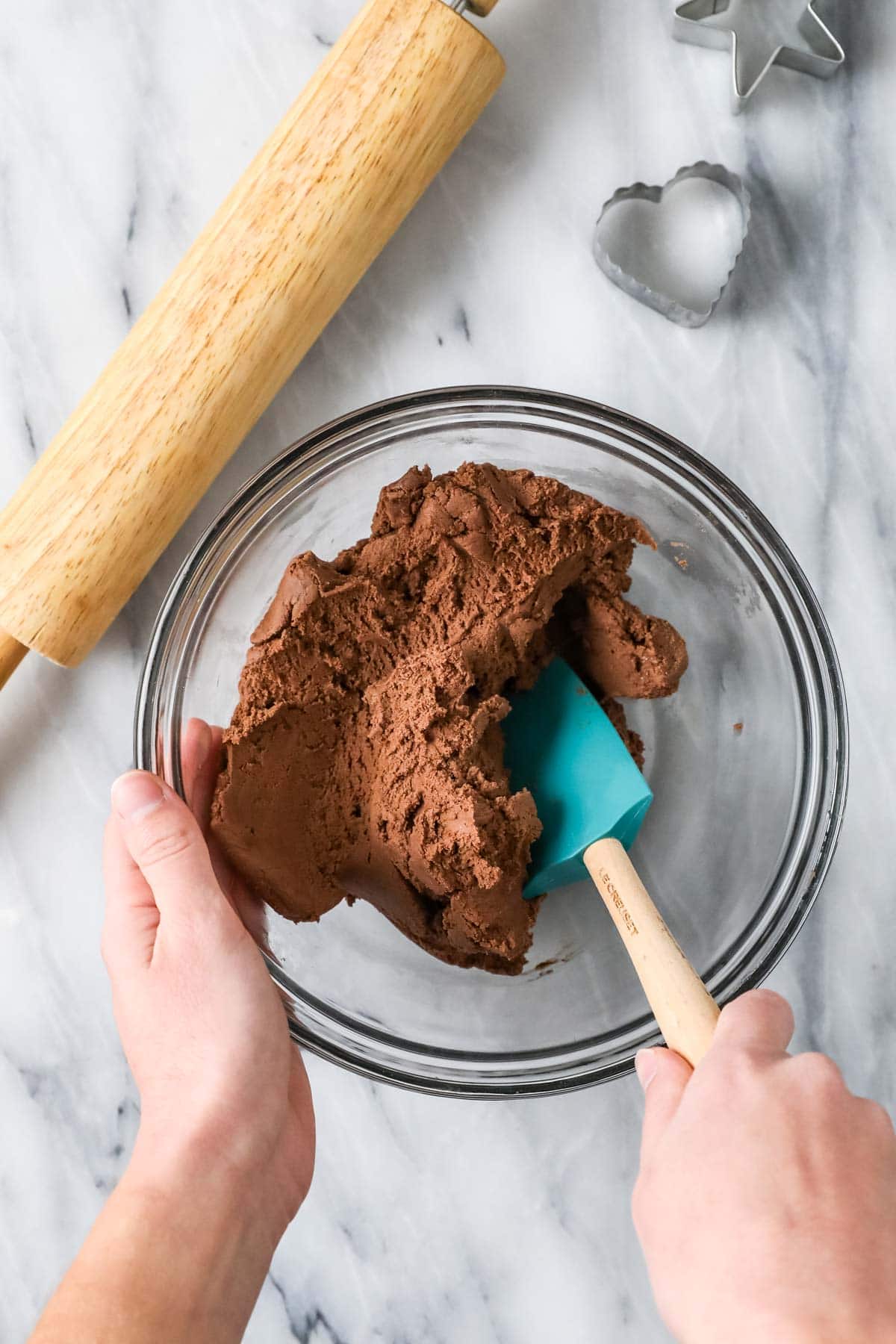 Overhead view of a bowl of chocolate cookie dough being stirred with a spatula.