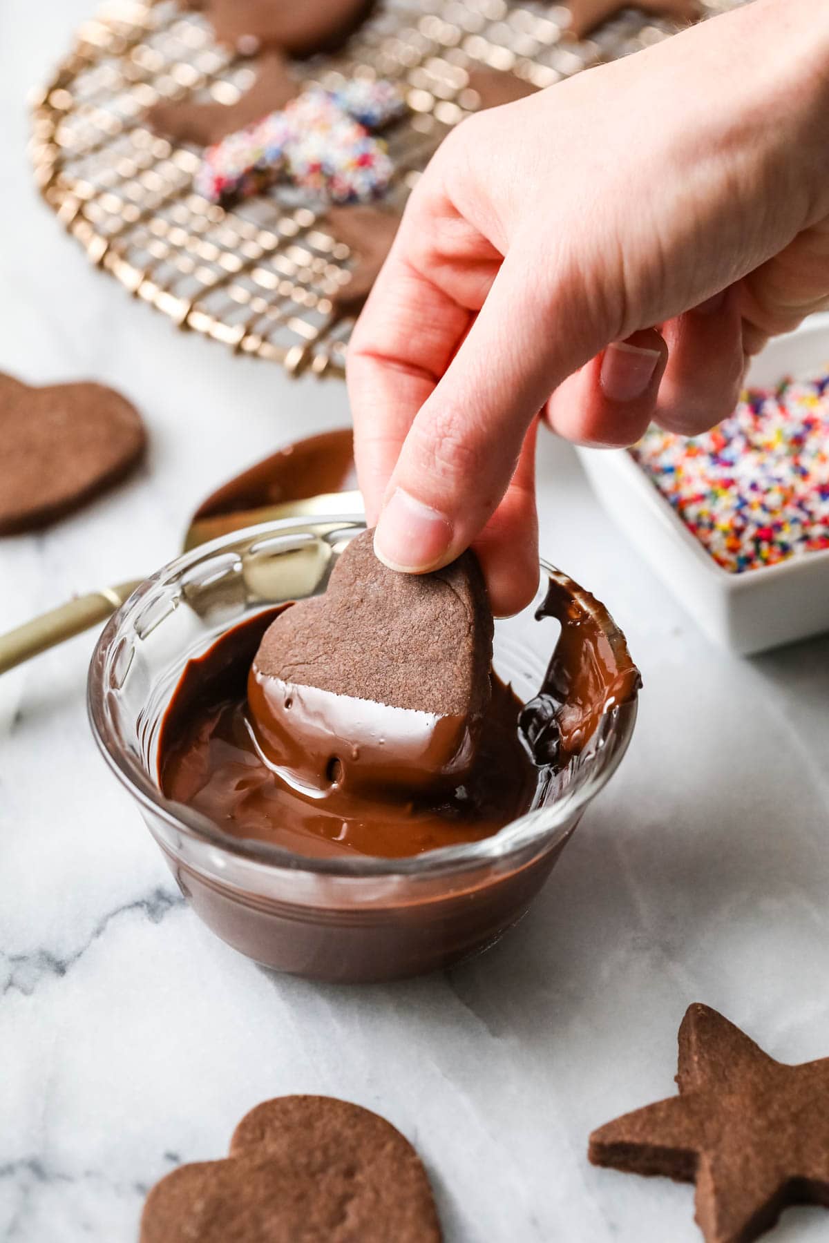 Heart shaped chocolate shortbread cookie being half dipped in melted chocolate.