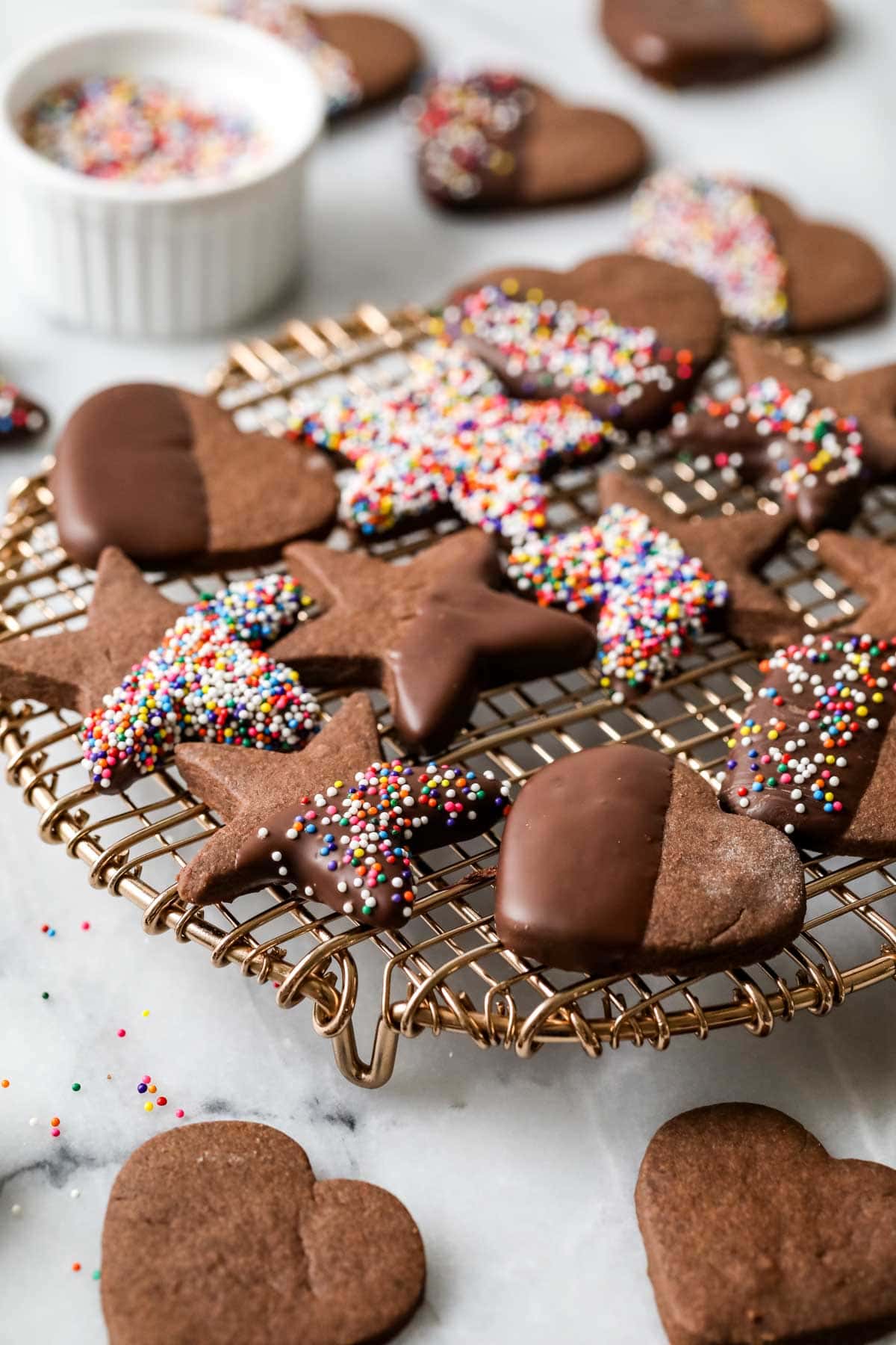 Cooling rack of chocolate shortbread cookies with some that have been dipped in chocolate and covered in colorful nonpareil sprinkles.