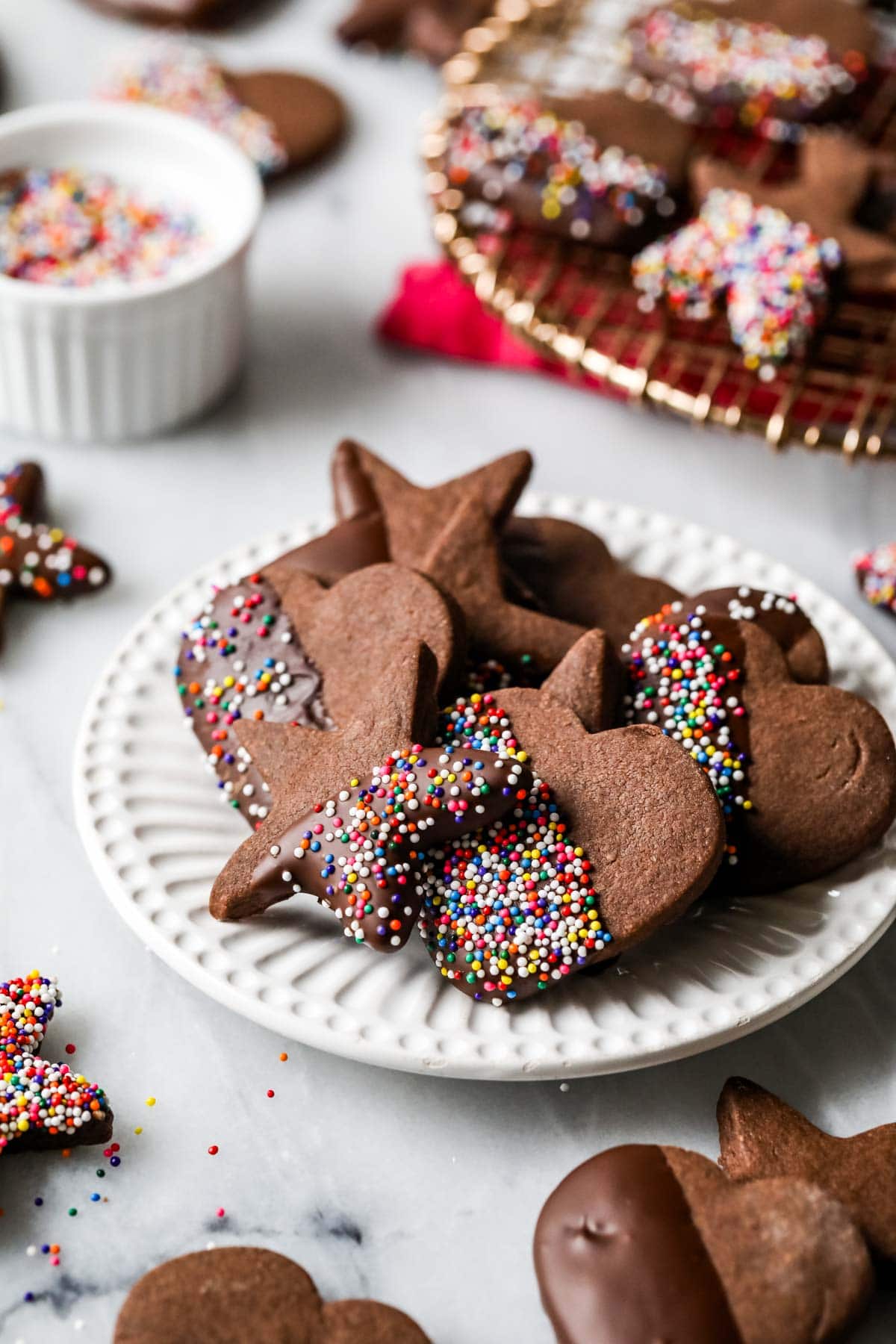 Plate of chocolate shortbread cookies that have been half dipped in chocolate and nonpareil sprinkles.