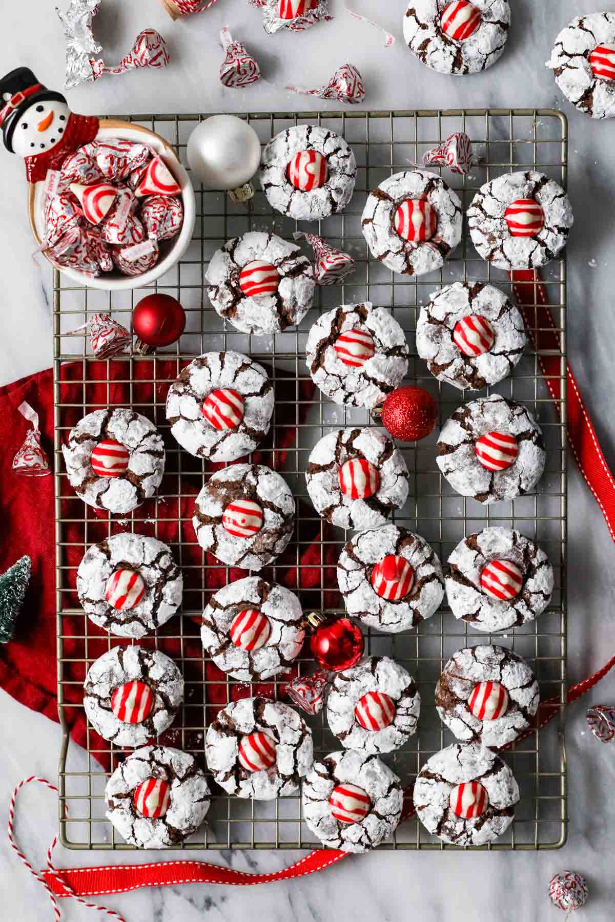 Overhead view of chocolate Christmas cookies coated in powdered sugar and topped with candy cane kisses.