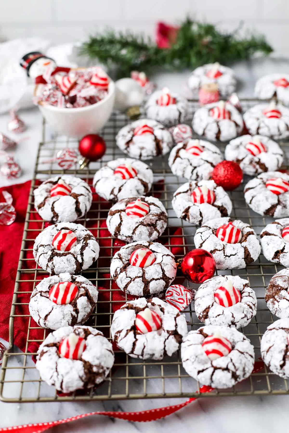 Chocolate Christmas cookies coated in powdered sugar and topped with candy cane kisses on a cooling rack.