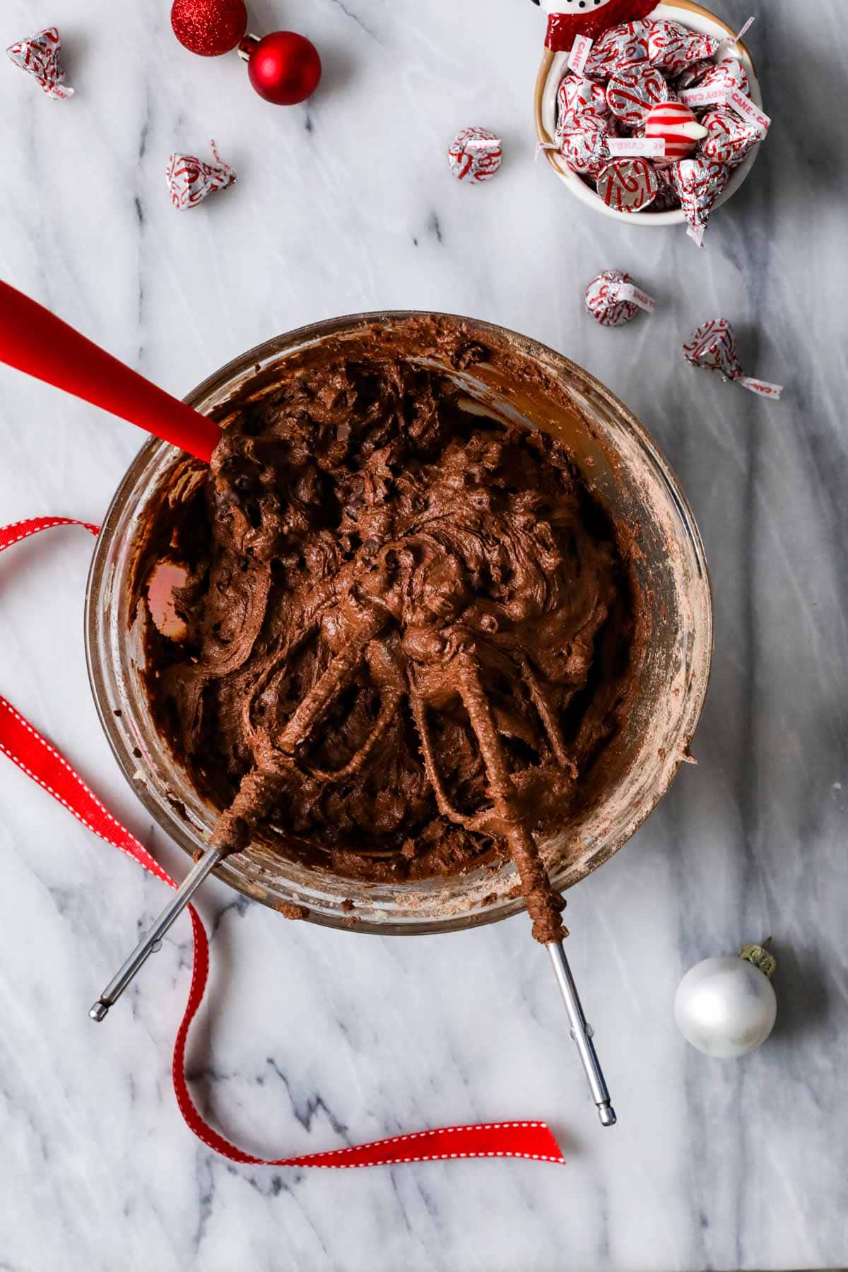 Overhead view of a bowl of chocolate cookie dough with two dough covered beaters on top.