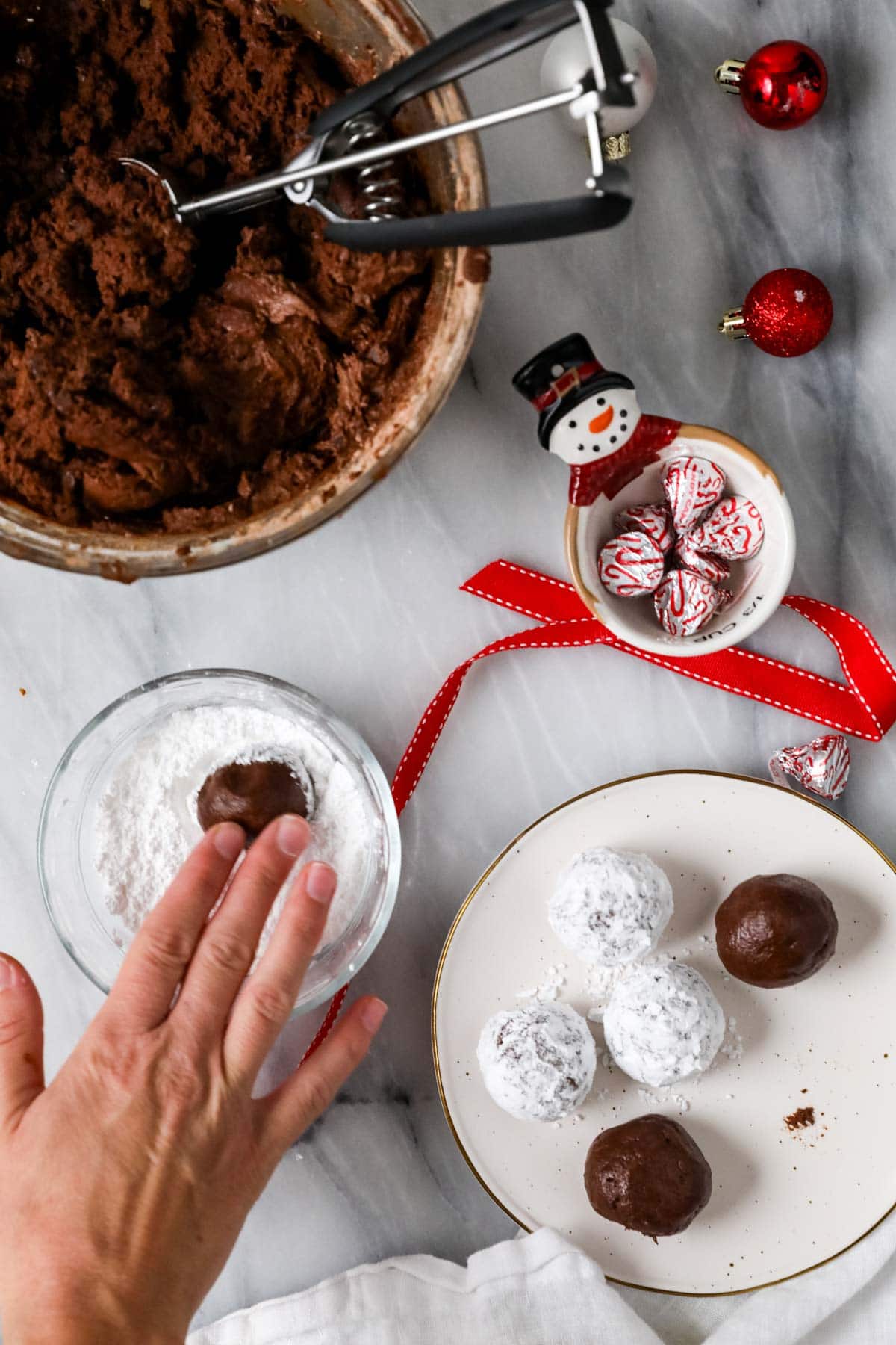 Hands rolling chocolate cookie dough balls in powdered sugar.