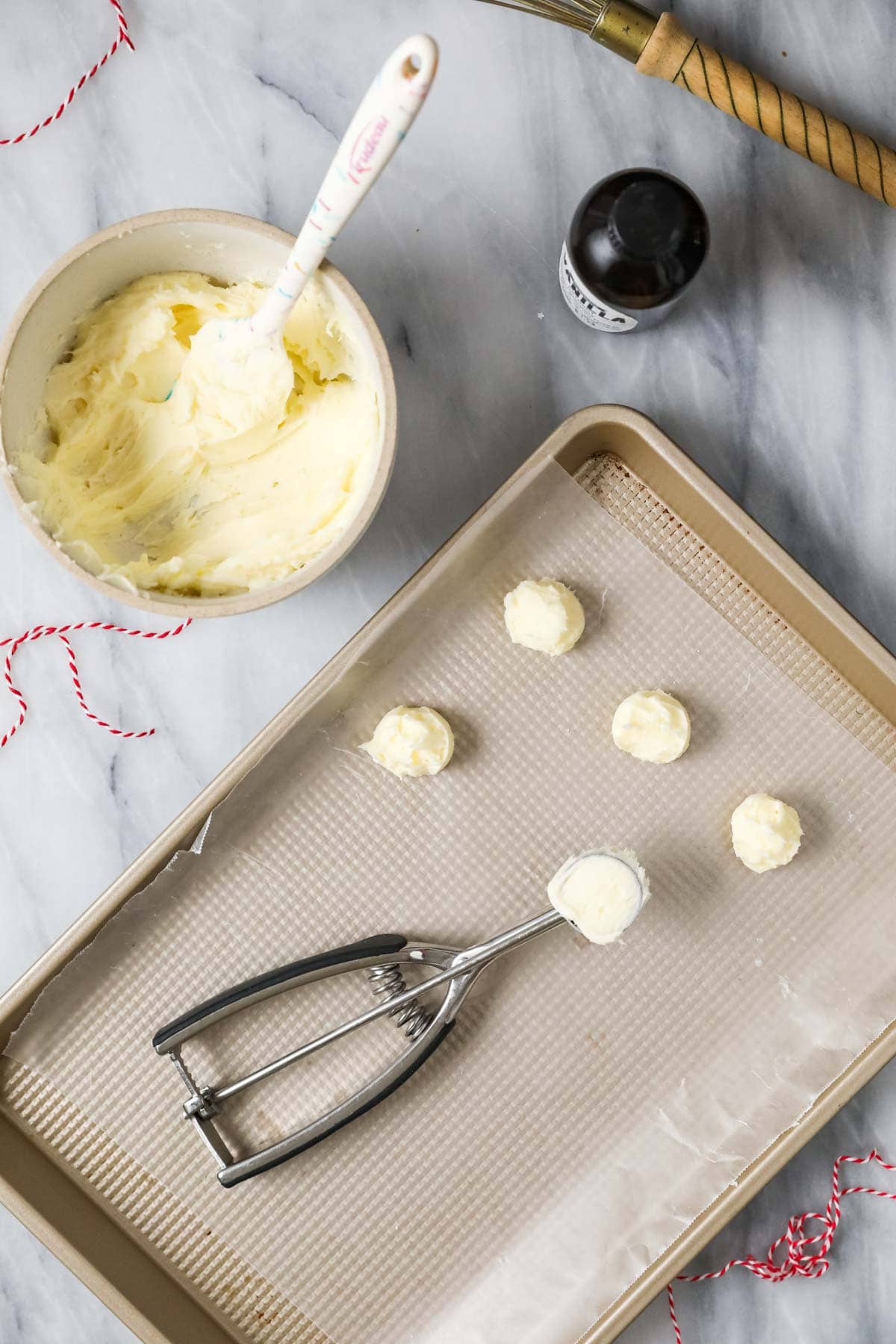 Overhead view of dollops of buttercream frosting being dropped on a wax paper lined baking sheet.