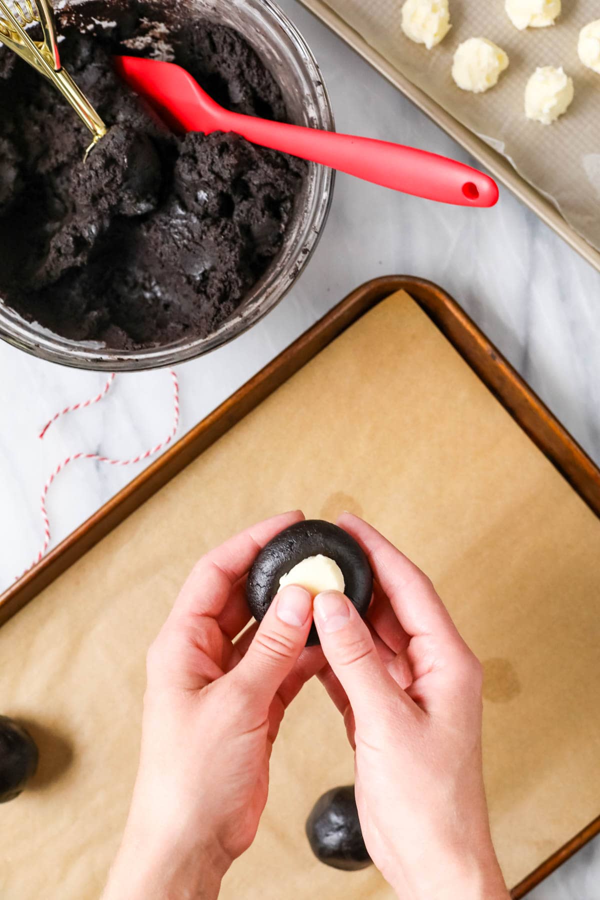 Hand pressing a frozen dollop of buttercream frosting into a black cocoa cookie dough.