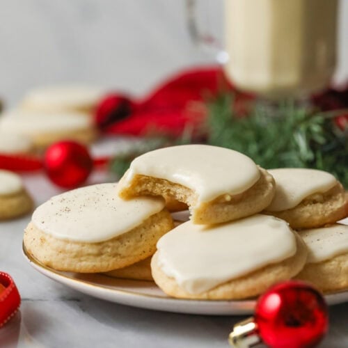 Plate of frosted eggnog cookies with a bite missing from the center cookie.