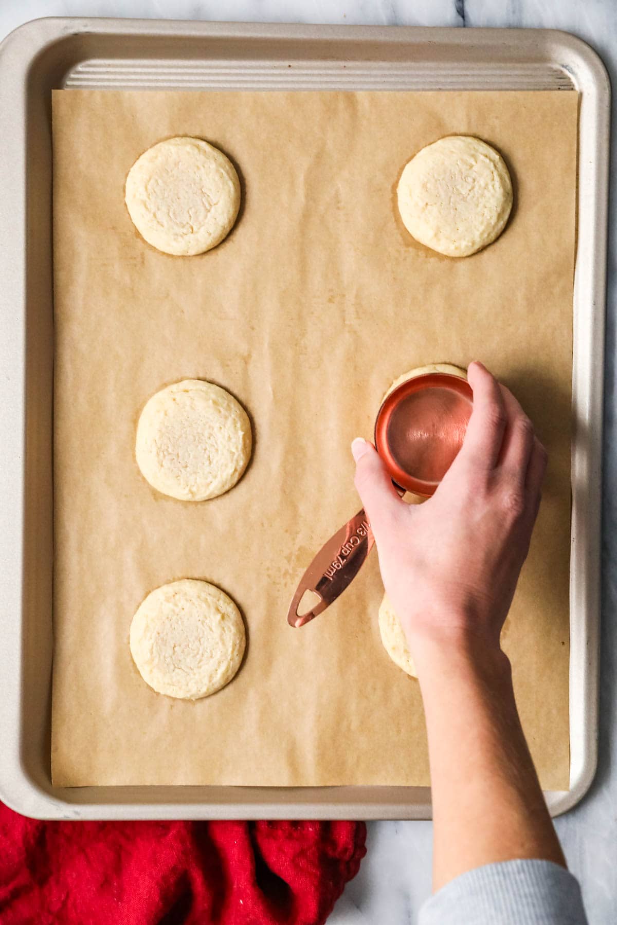 Overhead view of cookies being flattened with the bottom of a measuring cup.