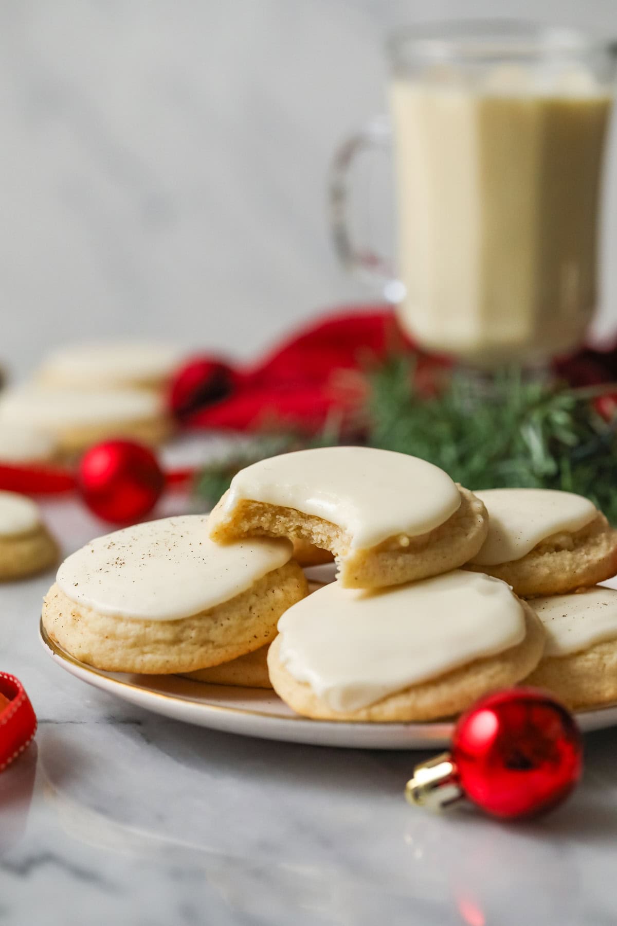 Plate of frosted eggnog cookies with a bite missing from the center cookie.