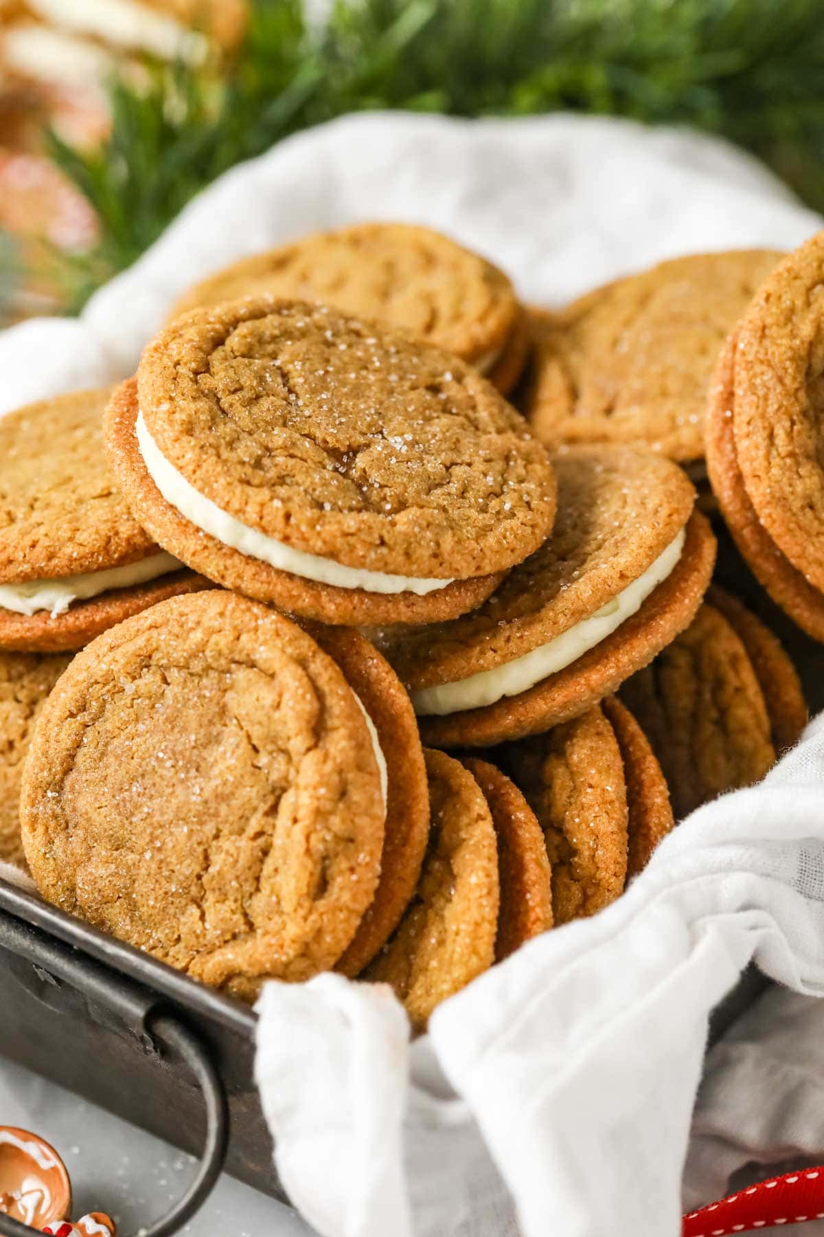 Pile of gingerbread sandwich cookies in a parchment lined metal tin.