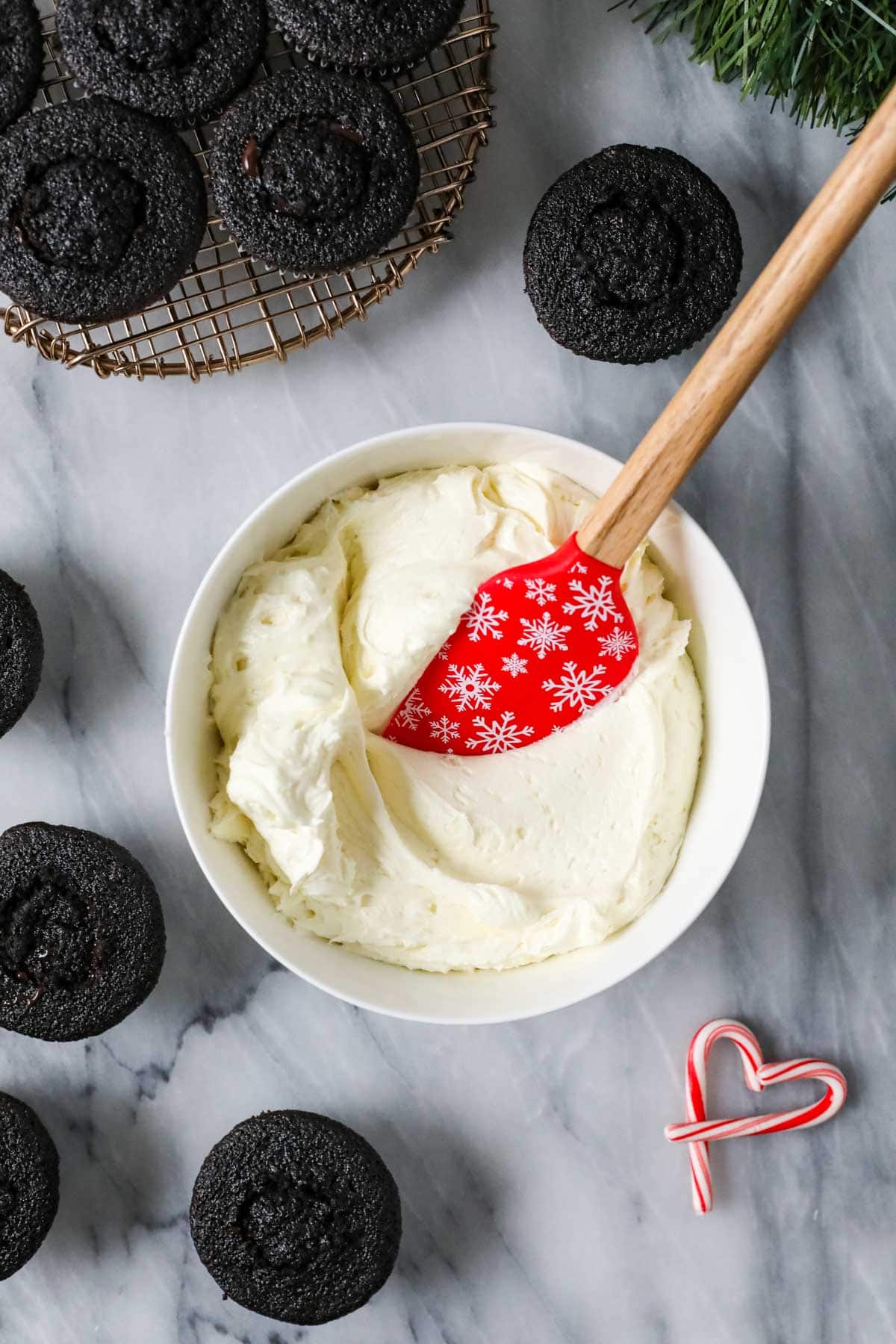 Red snowflake spatula in a bowl of peppermint white chocolate buttercream.