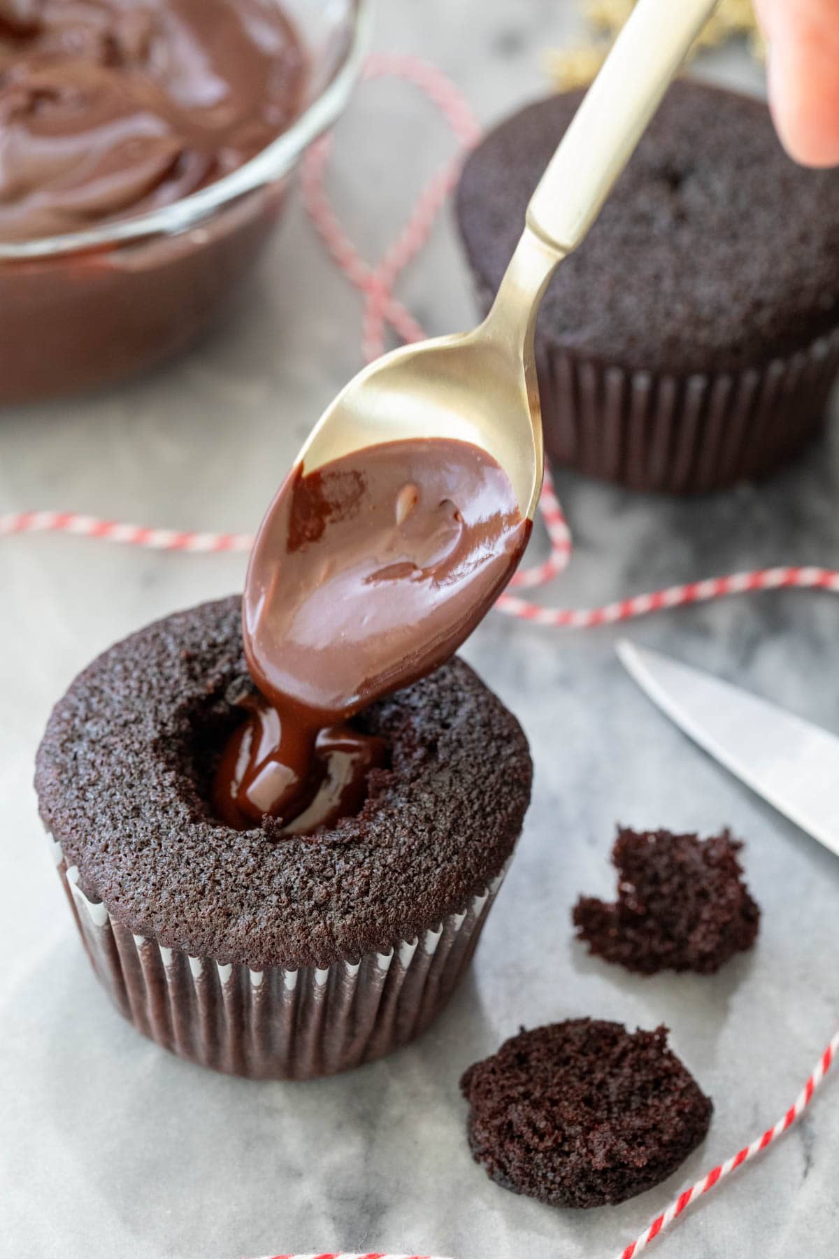 Chocolate ganache being poured into the center of a dark chocolate cupcake.