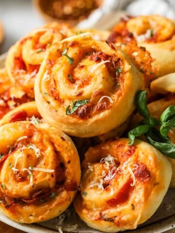 Pile of pizza rolls on a plate with fresh basil and parmesan on top.