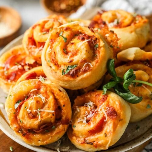 Pile of pizza rolls on a plate with fresh basil and parmesan on top.