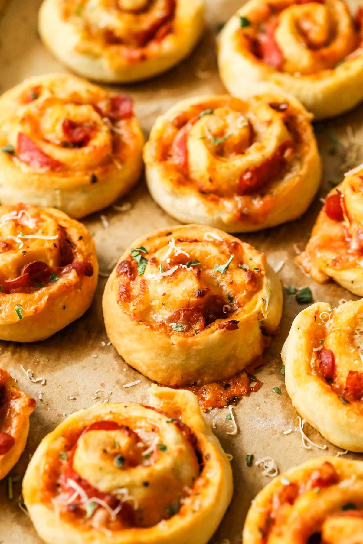 Rows of swirled rolls made with pizza sauce and cheese on a baking sheet.