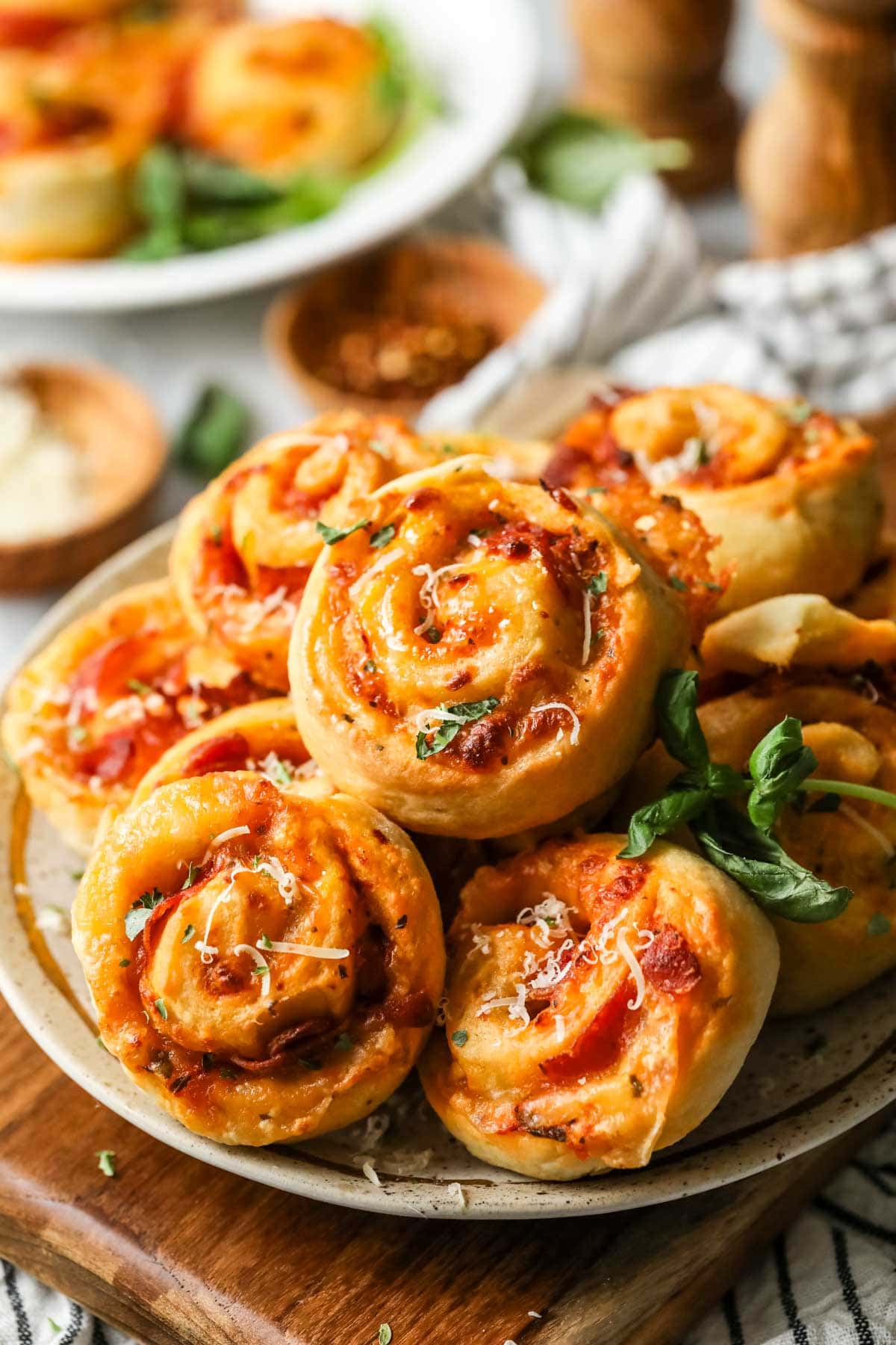 Pile of pizza rolls on a plate with fresh basil and parmesan on top.