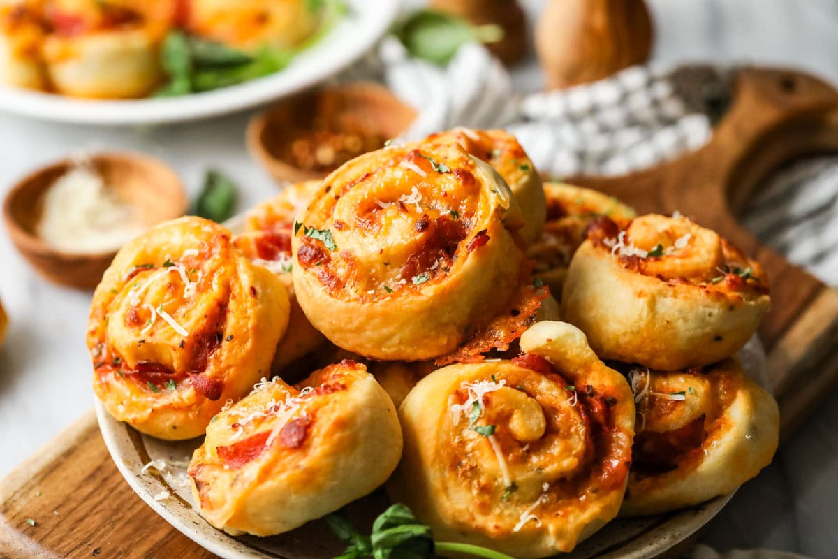 Pile of pizza rolls on a plate with fresh basil and parmesan on top.