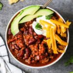 Overhead view of a bowl of turkey chili topped with avocado, shredded cheese, and sour cream.