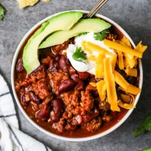 Overhead view of a bowl of turkey chili topped with avocado, shredded cheese, and sour cream.