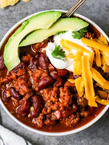 Overhead view of a bowl of turkey chili topped with avocado, shredded cheese, and sour cream.