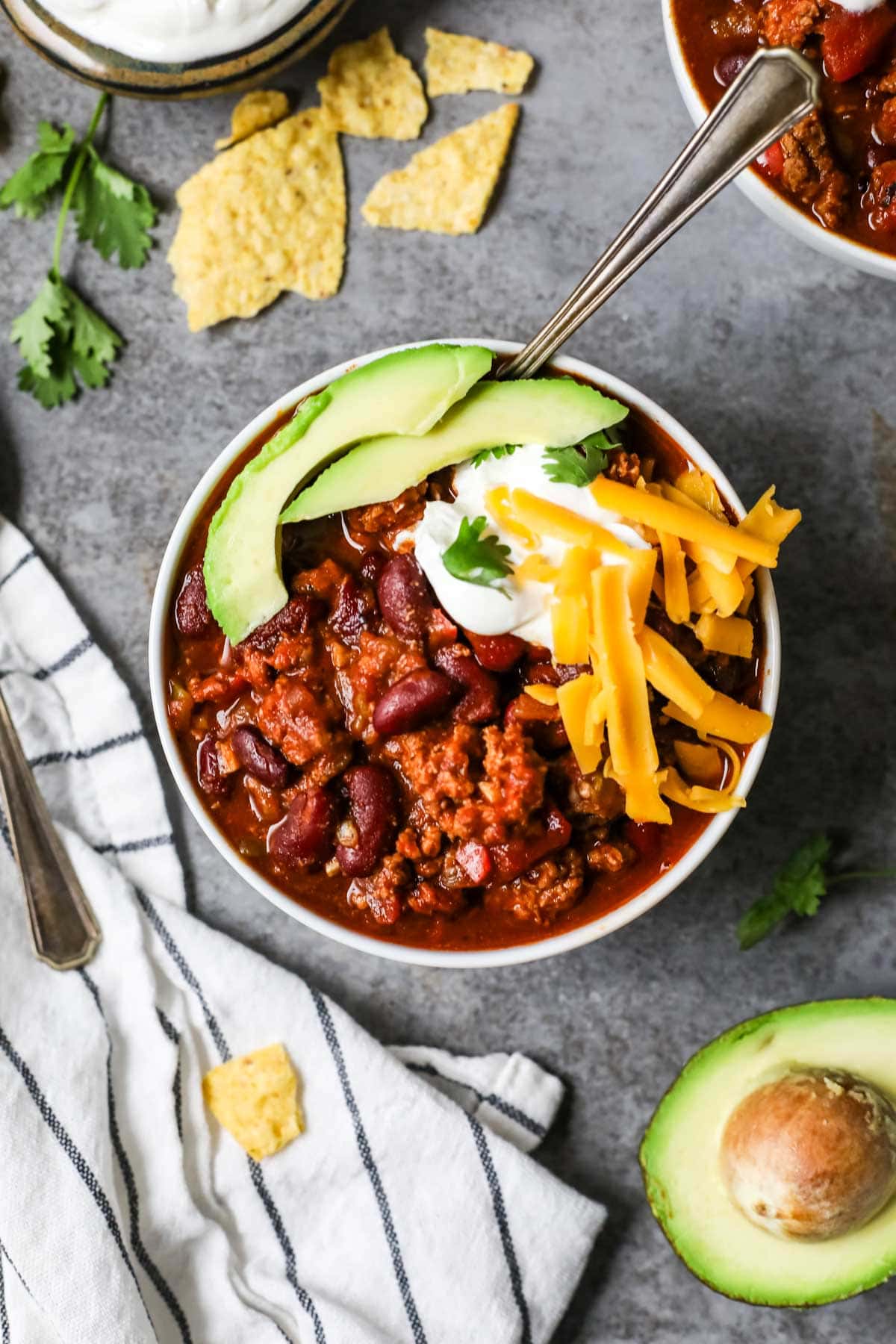 Overhead view of a bowl of turkey chili topped with avocado, shredded cheese, and sour cream.